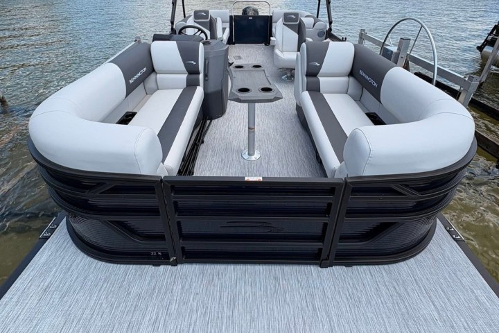 Pontoon boat with gray seating on a lake under a partly cloudy sky.