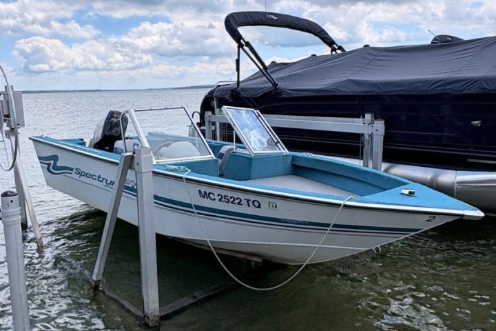 Small blue and white boat on a lift beside another covered boat.