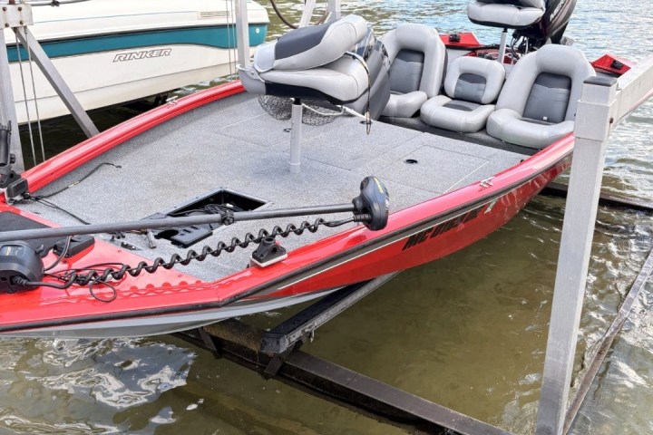 Red and gray fishing boat on a lift at a lakeside dock.