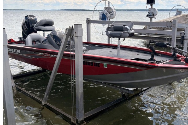 Red and gray boat docked on a lift near lakeside under cloudy sky.